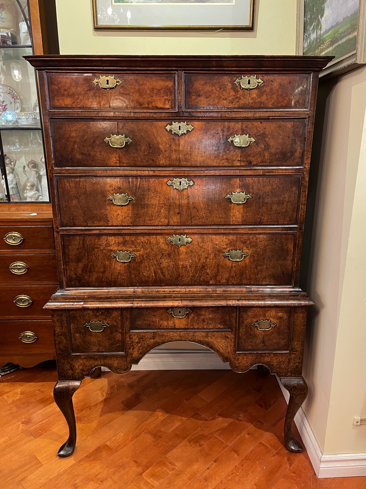 A Queen Anne figured walnut cross-banded chest on stand, rectangular shape,  moulded cornice above three short over three long gradual drawers with  brass scrolling drop handles and brass foliage escutcheon, raised on